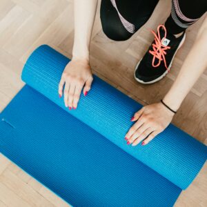 Overhead view of a woman preparing her blue yoga mat on a wooden floor, ready for exercise.